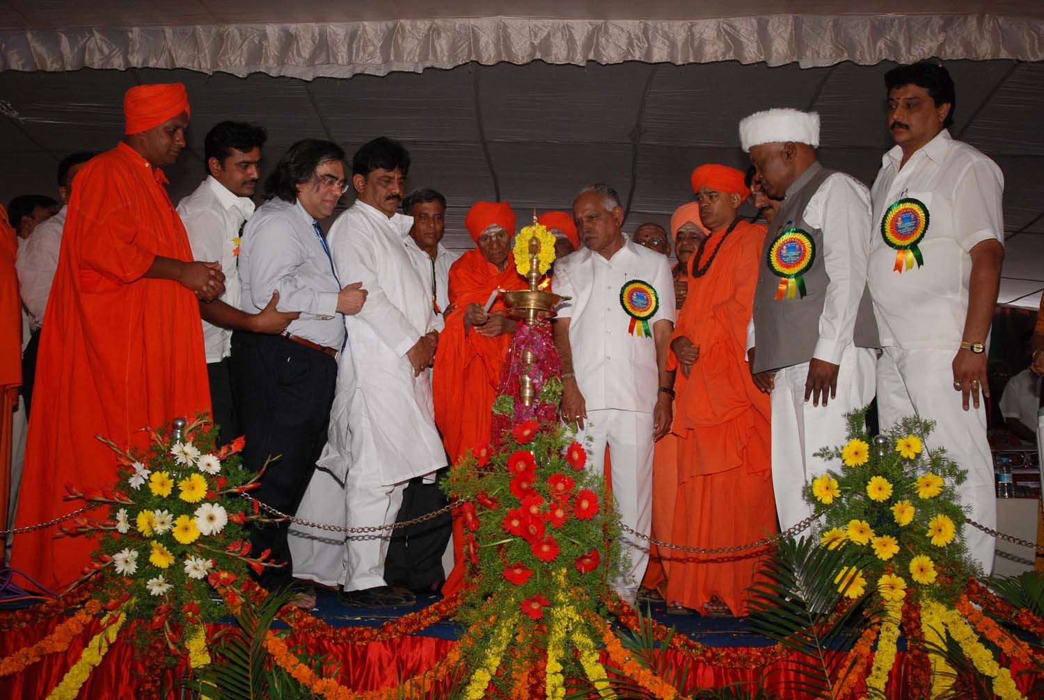 A ceremonial gathering with a Swamiji and public guests around a lamp