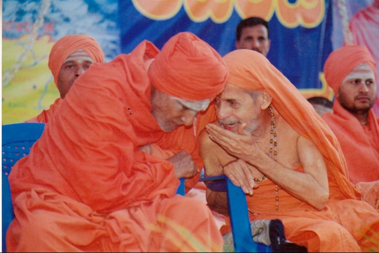 Two revered Swamijis sharing a close conversation during a gathering